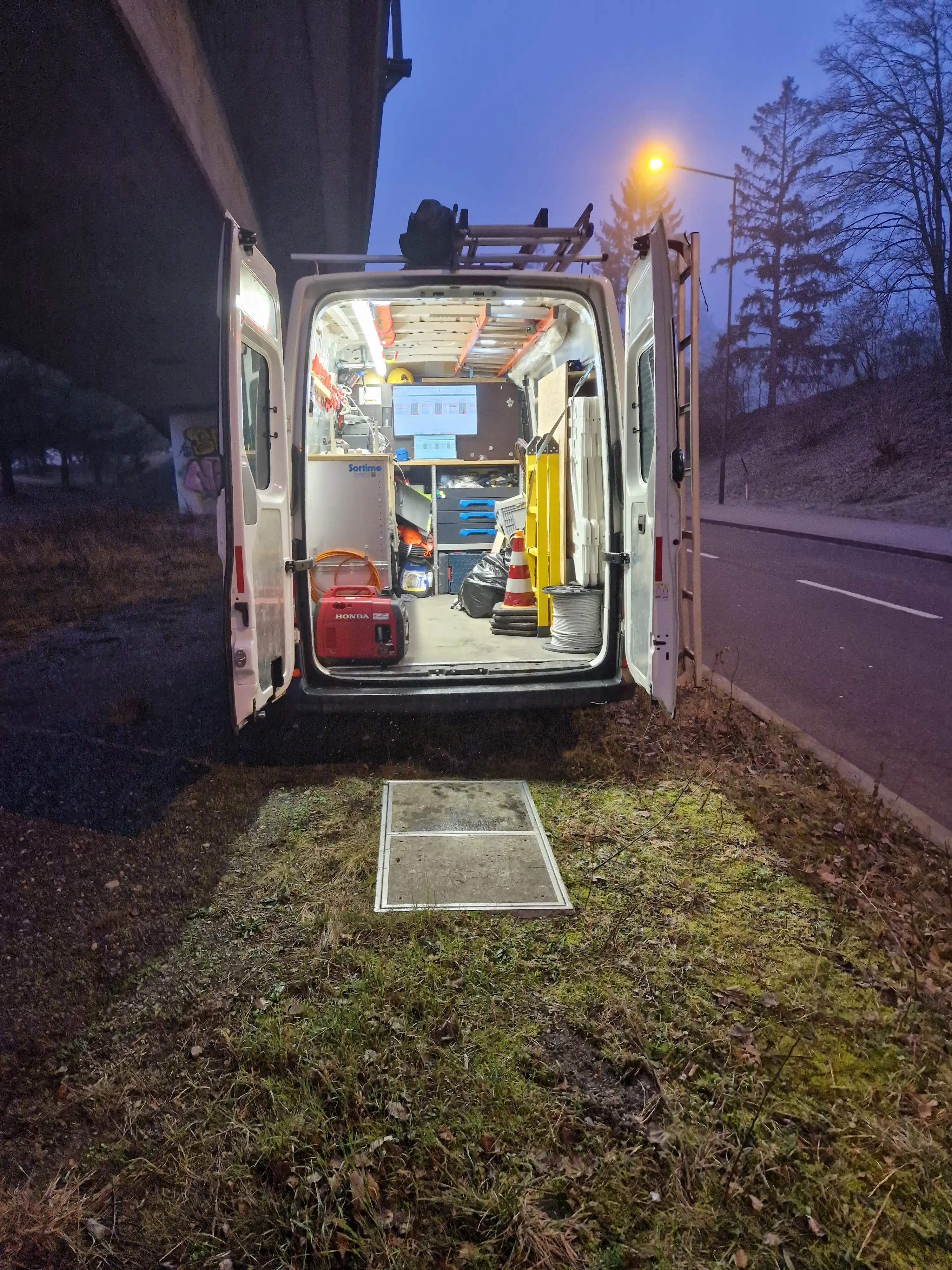 Servicefahrzeug mit geöffneten Türen im Morgengrauen bei einem Glasfaser-Einsatz an der Strasse